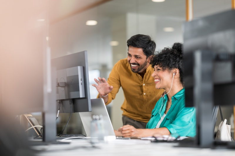 Two individuals collaborating on computers in a modern office setting.