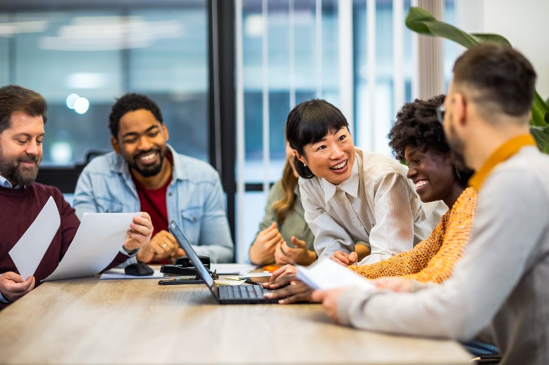 Group of people talking and smiling around a desk and laptop by Urban Office
