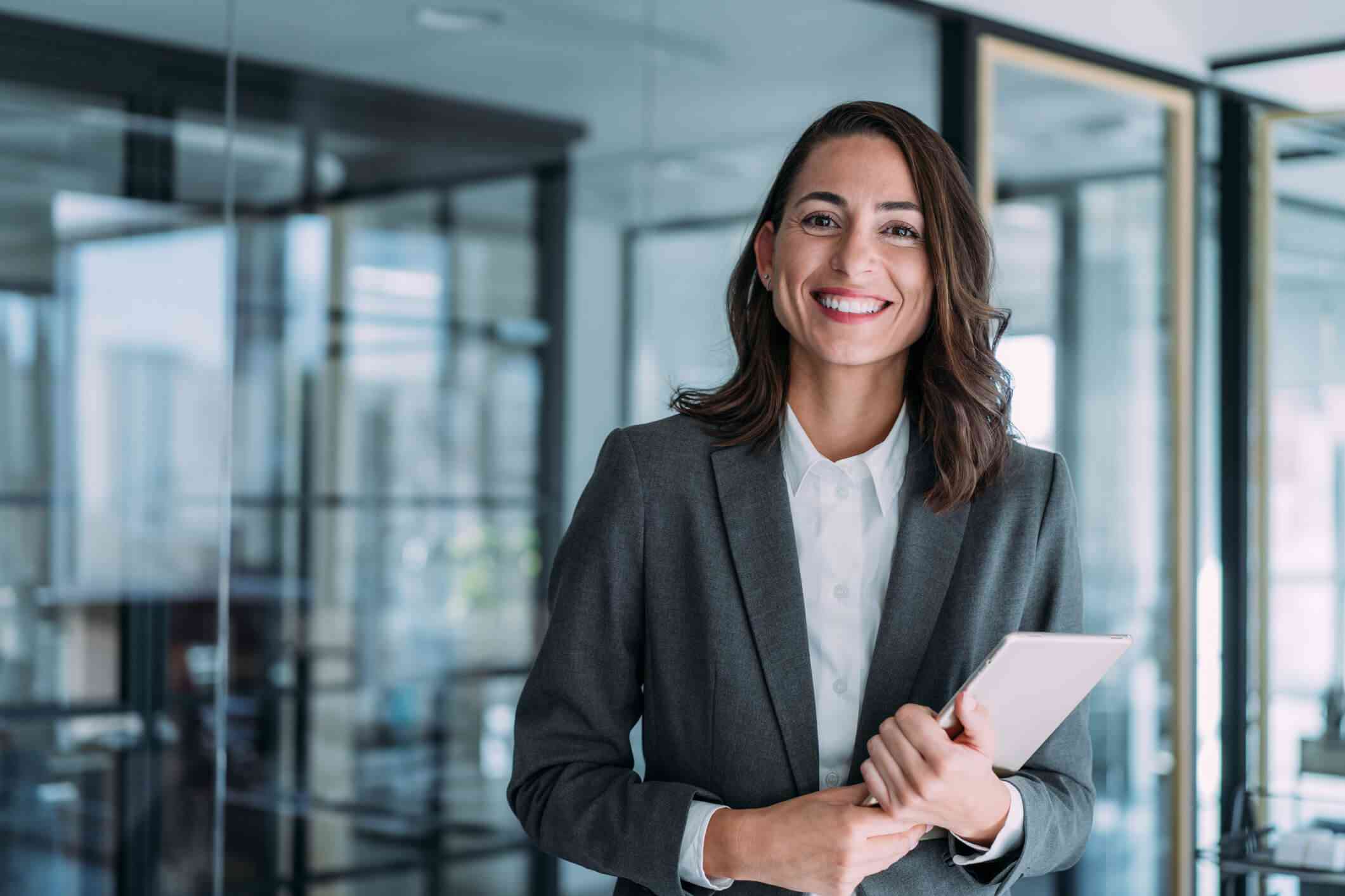 A businesswoman in a gray suit holding a tablet, standing in a modern office in Houston, TX