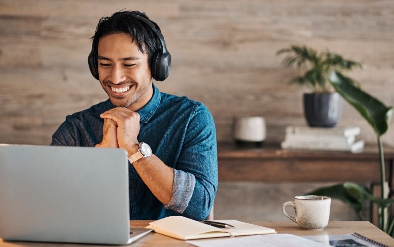 Smiling man wearing headphones, engaged with a laptop in a cozy workspace at an Urban Office space