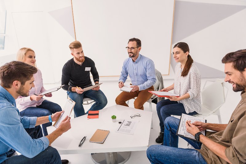 Group of people sitting around a table in a huddle by Urban Office